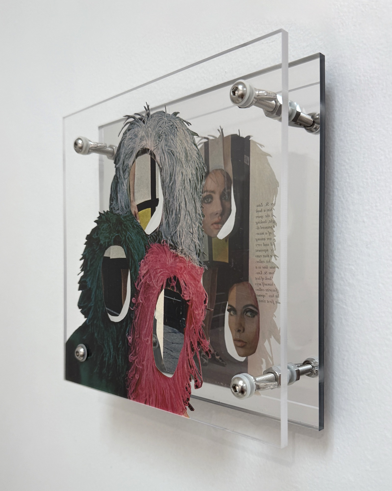 Adornment by Shannon Milar — Double Take series. Found images, clear + mirrored acrylic, nylon + metal hardware. Large feathered forms in teal and pink frame openings through which faces are glimpsed, the mirrored backing reflecting printed text.