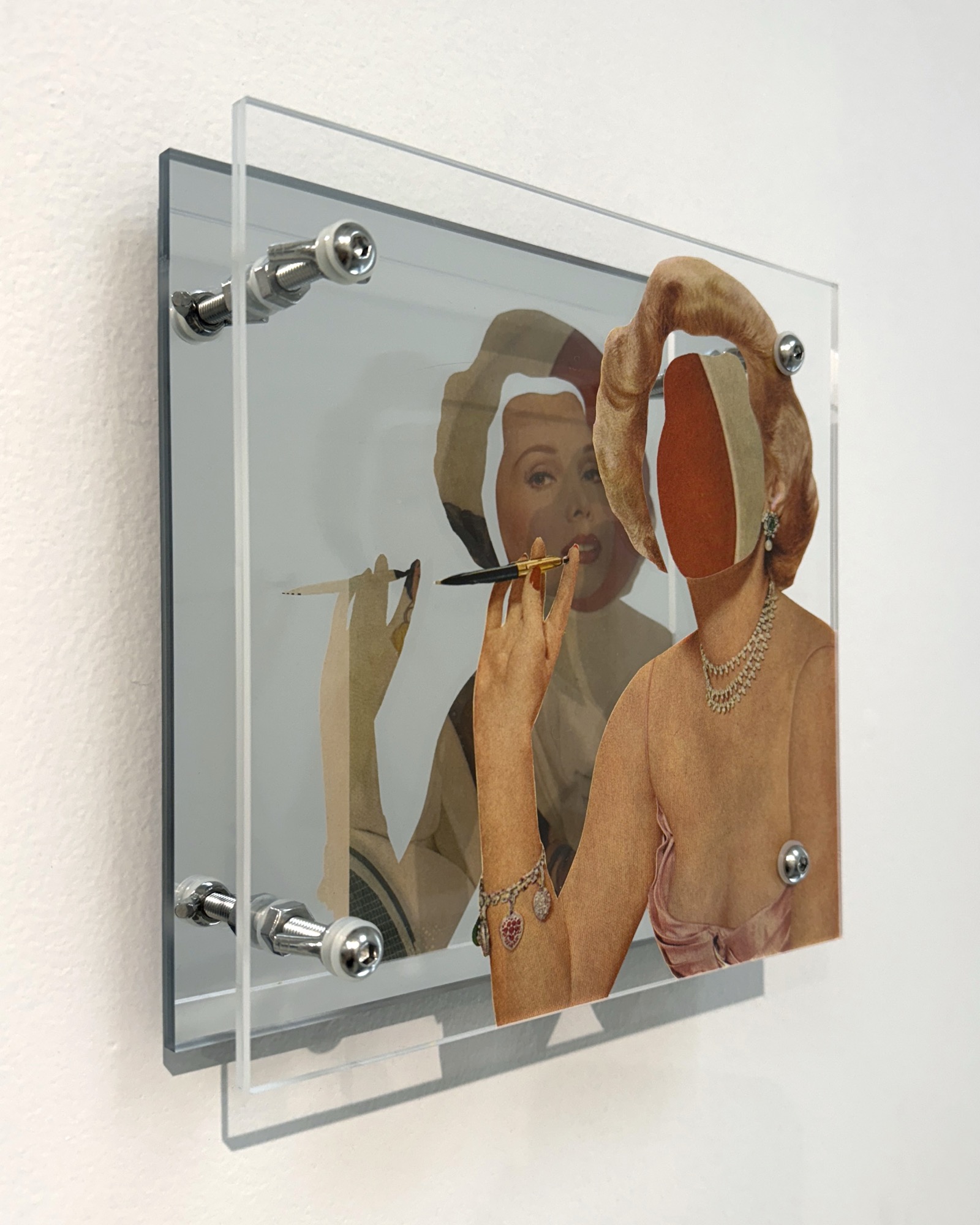 Precision by Shannon Milar — Double Take series. Found images, clear + mirrored acrylic, nylon + metal hardware. A figure applying a cosmetic, face replaced by a cutout showing the page back, charm bracelet and pearl necklace visible, the mirror doubling the gesture.