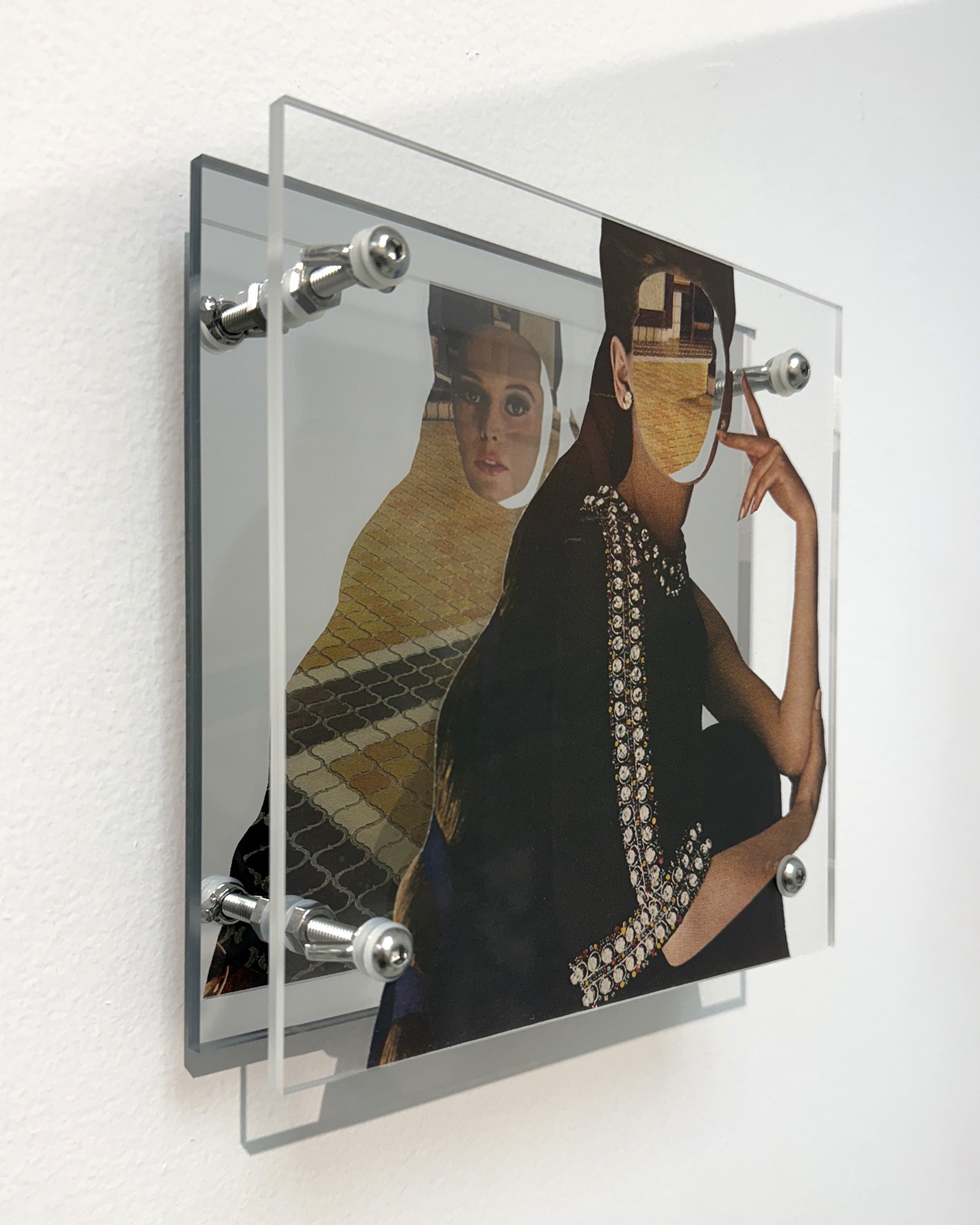 Surface by Shannon Milar — Double Take series. Found images, clear + mirrored acrylic, nylon + metal hardware. Two figures — one in geometric sunglasses, one in a jeweled garment — layered over a patterned fabric ground, the mirror revealing the back of the printed page.
