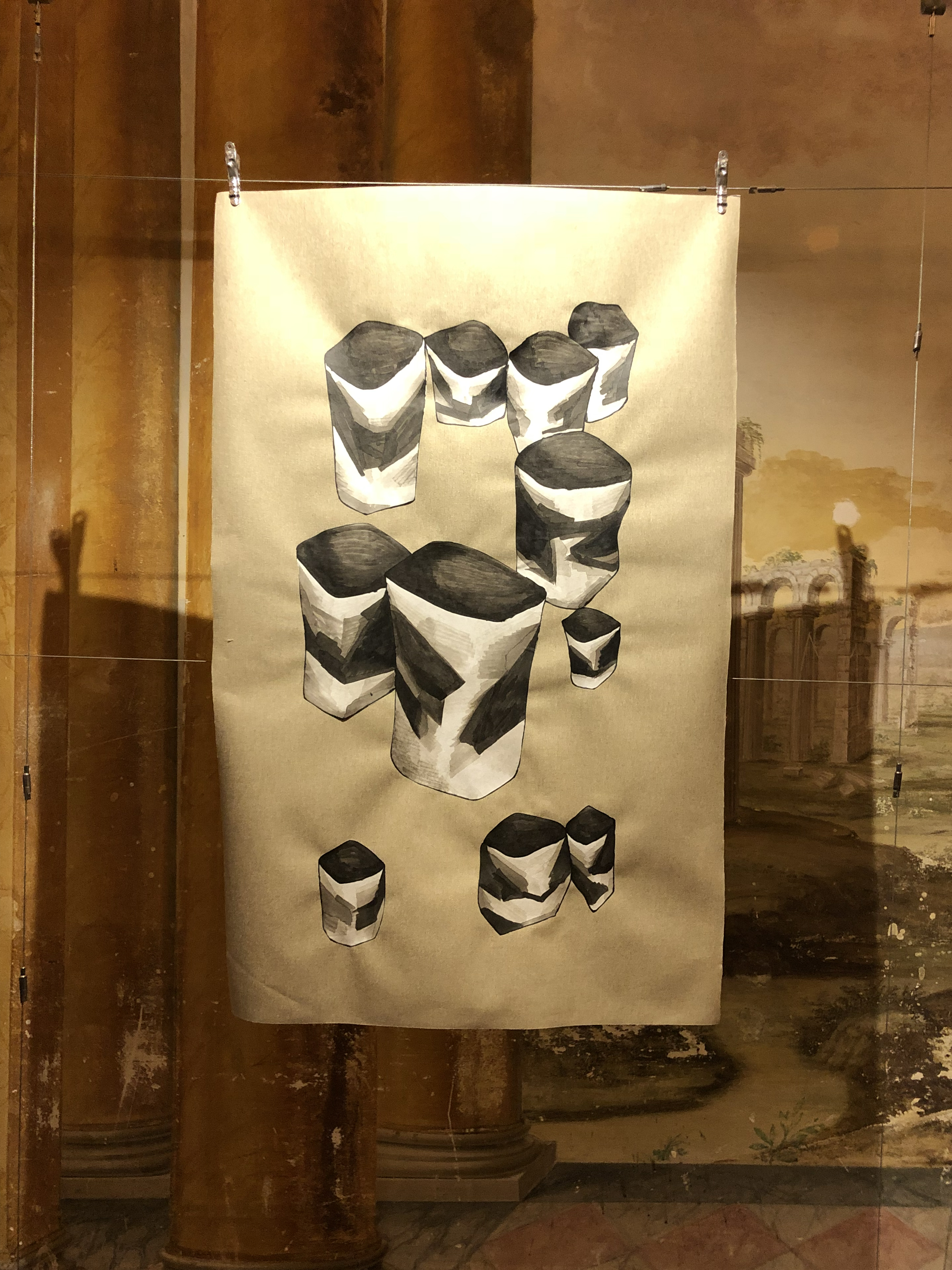Cups by Shannon Milar — Life Inflamed series. Ink on paper, 2018. Installation view at Villa Bottini, Lucca. A large drawing on natural paper, clipped to wire and suspended before the villa's sfumato fresco walls. Multiple cup and vessel forms in bold black ink with gestural white highlighting, ranging from large at centre to smaller forms below, their cylindrical volumes slightly angular. The ochre-toned architectural fresco is visible behind.