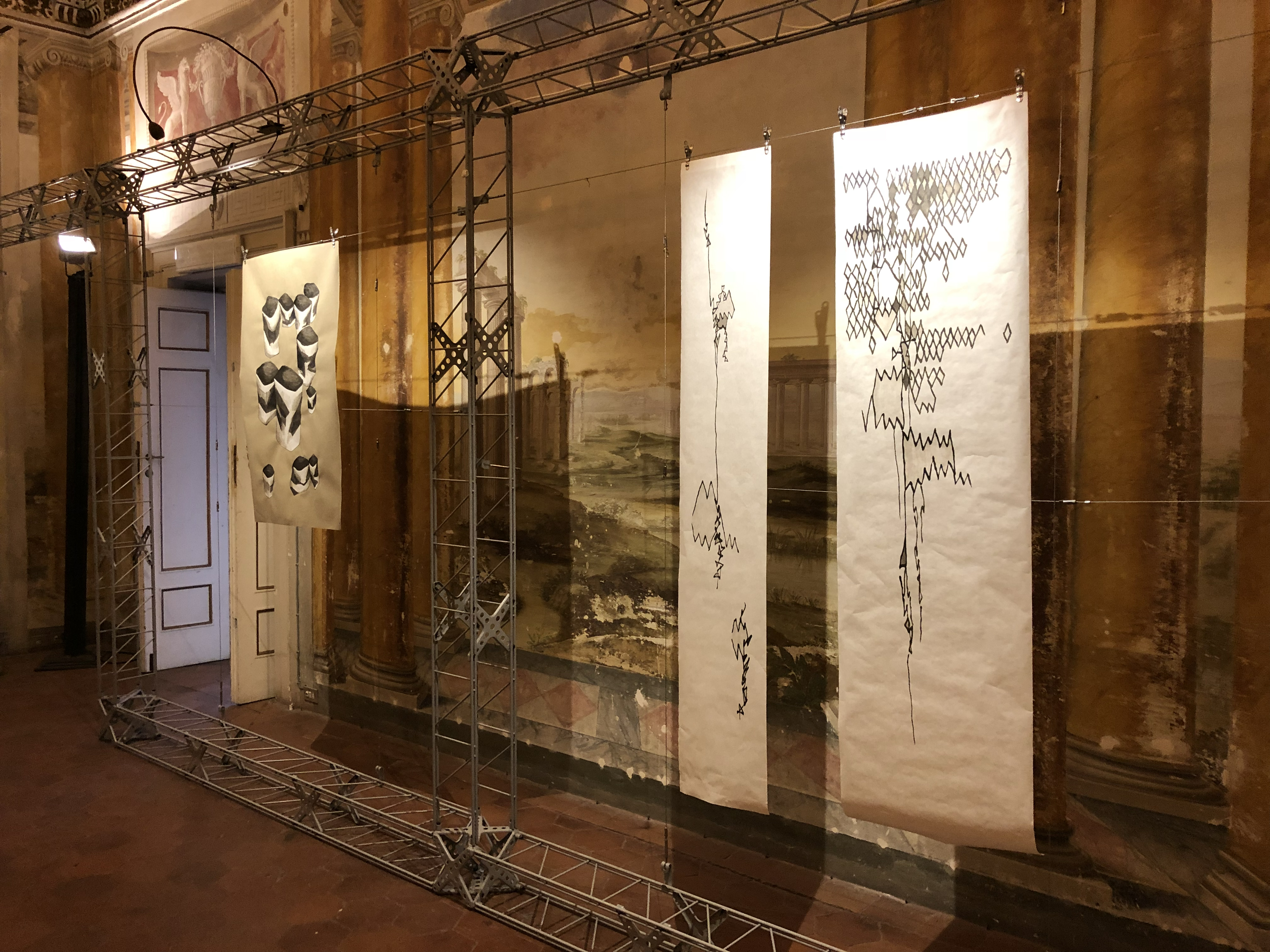 Life Inflamed installation view, Villa Bottini, Lucca, 2018. Shannon Milar. Three large ink drawings on paper suspended on a metal scaffold frame before the fresco walls. From left: Cups, a drawing of vessel forms, and Lines 1 and Lines 2, two tall vertical sheets of descending ink marks. The scaffold stands in front of the villa's seascape and architectural fresco, the sparse marks of the drawings in direct contrast to the layered permanence of the painted interior.